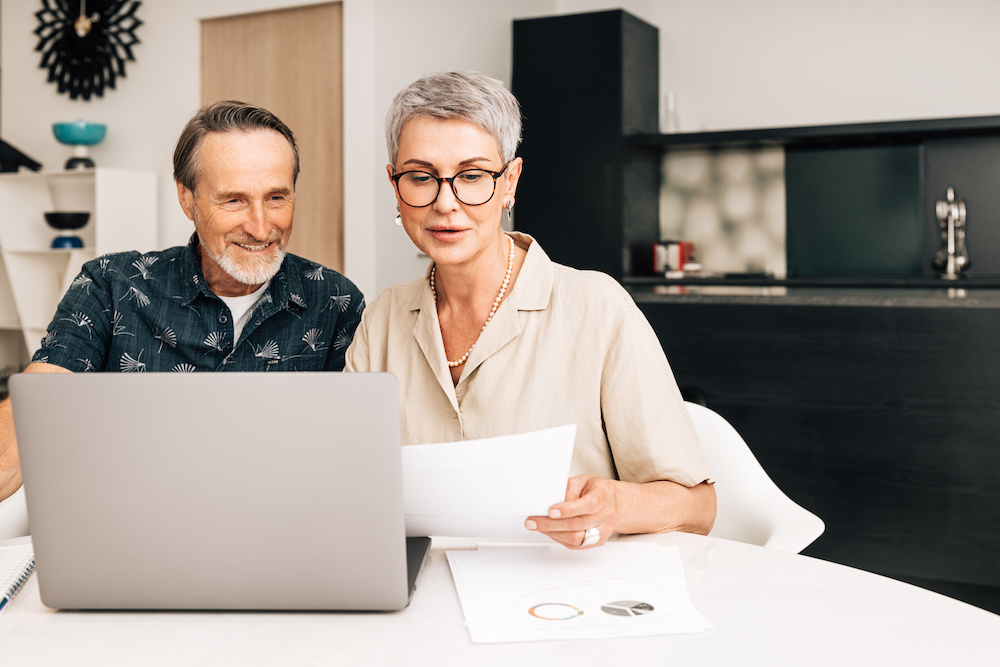 Creating a Tax-Efficient Retirement Strategy: Tips from Financial Experts | Flynn Wealth Partners Senior retired couple at a table in dining room using a laptop computer. Two mature people looking at paperwork and discussing their finances.